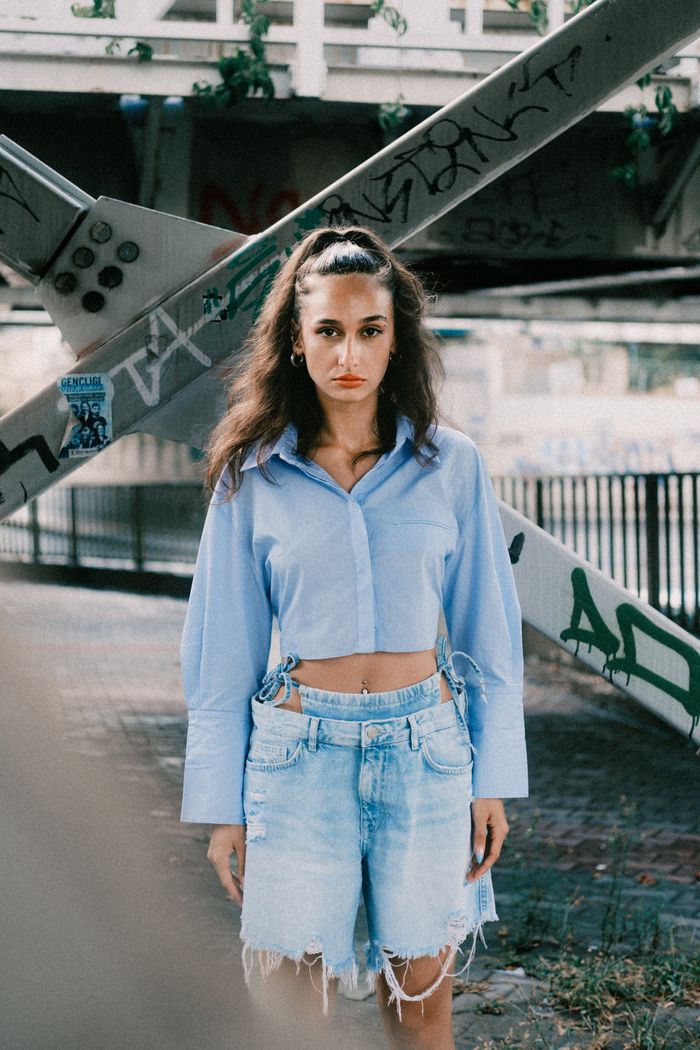 Stylish woman in a blue blouse and denim shorts standing under an urban bridge.