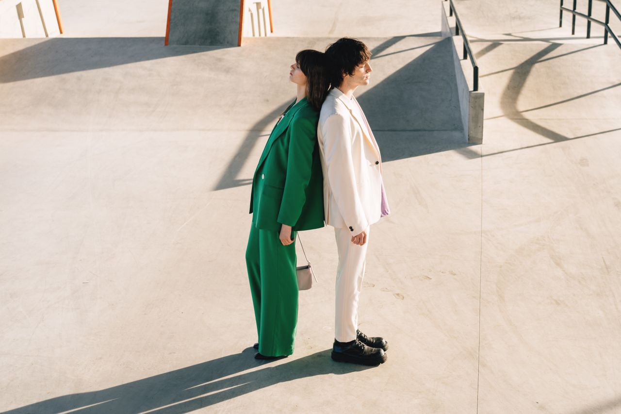 A fashionable couple in vibrant suits standing back-to-back in an urban space.